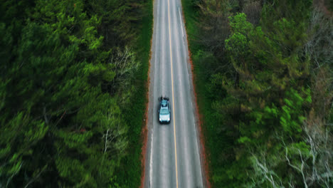 aerial top down view of car reveal driving down empty forest road surrounded by trees cinematic drone travel adventure vacation 4k