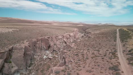 Drone-Pasando-Entre-Un-Camino-De-Grava-Y-Un-Pequeño-Cañón-En-El-Desierto-Chileno