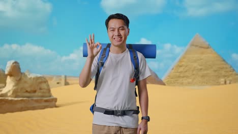 man with backpack showing ok sign in front of pyramids