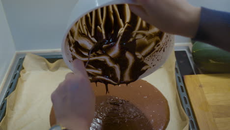 manos de mujer vertiendo masa de brownie en una bandeja para hornear