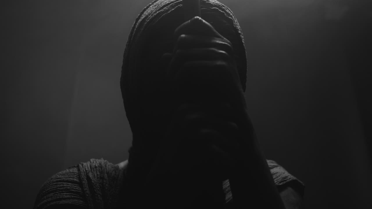 A mummified woman against the dark background pose with the walking staff