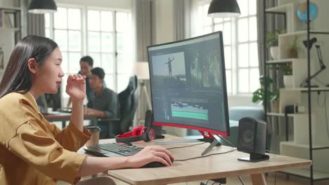 tired asian female video editor works with footage and sound on her personal computer in office
