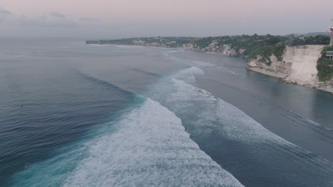 Drone-Del-Colapso-Del-Acantilado-De-Sobredesarrollo-En-La-Playa-De-Bingin,-Bali,-Uluwatu-Indonesia-Al-Atardecer-De-La-Hora-Dorada-Con-Olas-Y-Surfistas