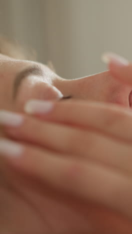 mujer joven golpea la piel con un parche nutritivo con los dedos en una habitación iluminada en cámara lenta. la mujer aplica almohadillas especiales debajo de los ojos para hidratar la piel de la cara