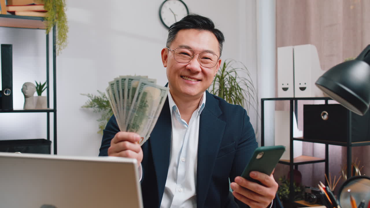 Happy rich asian businessman counting money cash use smartphone app earning profit success contract