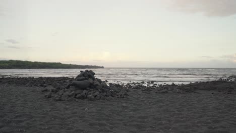 Gestapelte-Felsen-An-Einem-Schwarzen,-Einsamen-Schwarzen-Sandstrand-Bei-Sonnenuntergang