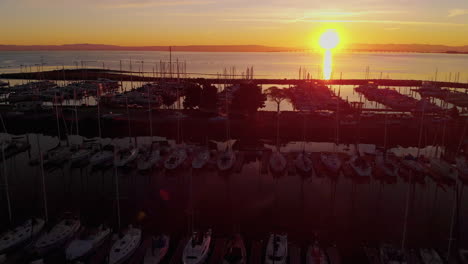 Sunrise-aerial-fly-over-of-a-boat-marina-at-sunrise,-in-the-california-Peninsula,-sea-birds,-sailing-vessels,-aerial-views-and-a-shining-morning-sun-reflecting-off-the-calm-SF-bay