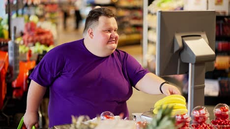 a happy overweight man in a purple t-shirt and short hair puts bananas on special scales in the supermarket to get a price tag on them and find out the weight of the fruit