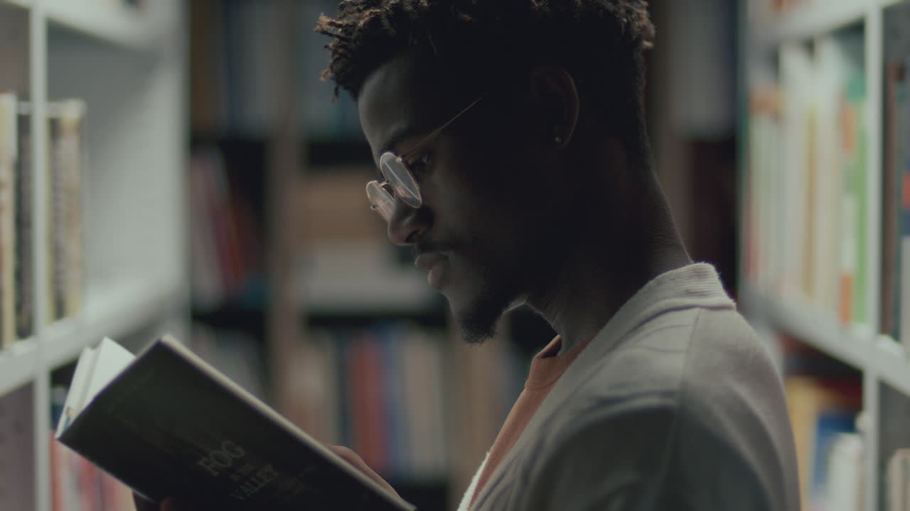 hombre afroamericano enfocado leyendo un libro en la biblioteca pública