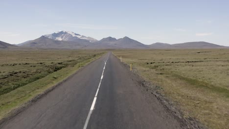 antena de vuelo bajo sobre camino rural vacío en islandia con montañas en segundo plano.