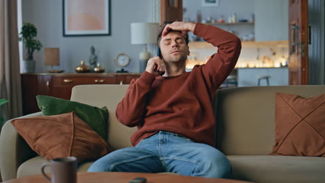puzzled man speaking smartphone hearing bad news on couch. guy feeling headache