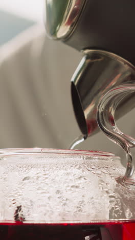 pouring boiling water from kettle into teapot closeup. brewing hibiscus tea enjoying aromatic steam of plant in kitchen. concept of relaxation