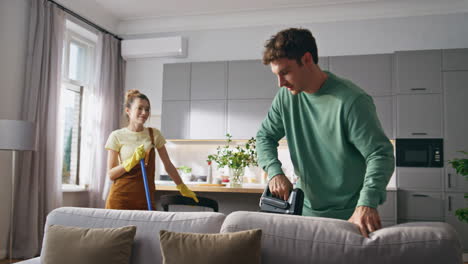 jonge echtgenoten huishoudelijke routine. positieve man stofzuigende bank praten gelukkige vrouw