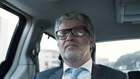 senior bearded businessman with suit and glasses, sitting in backseat of moving car