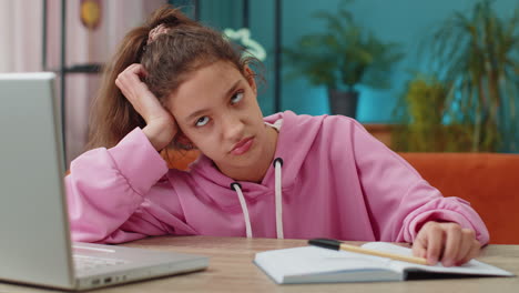 bored tired school girl doing homework exercise online typing on laptop makes notes in notebook