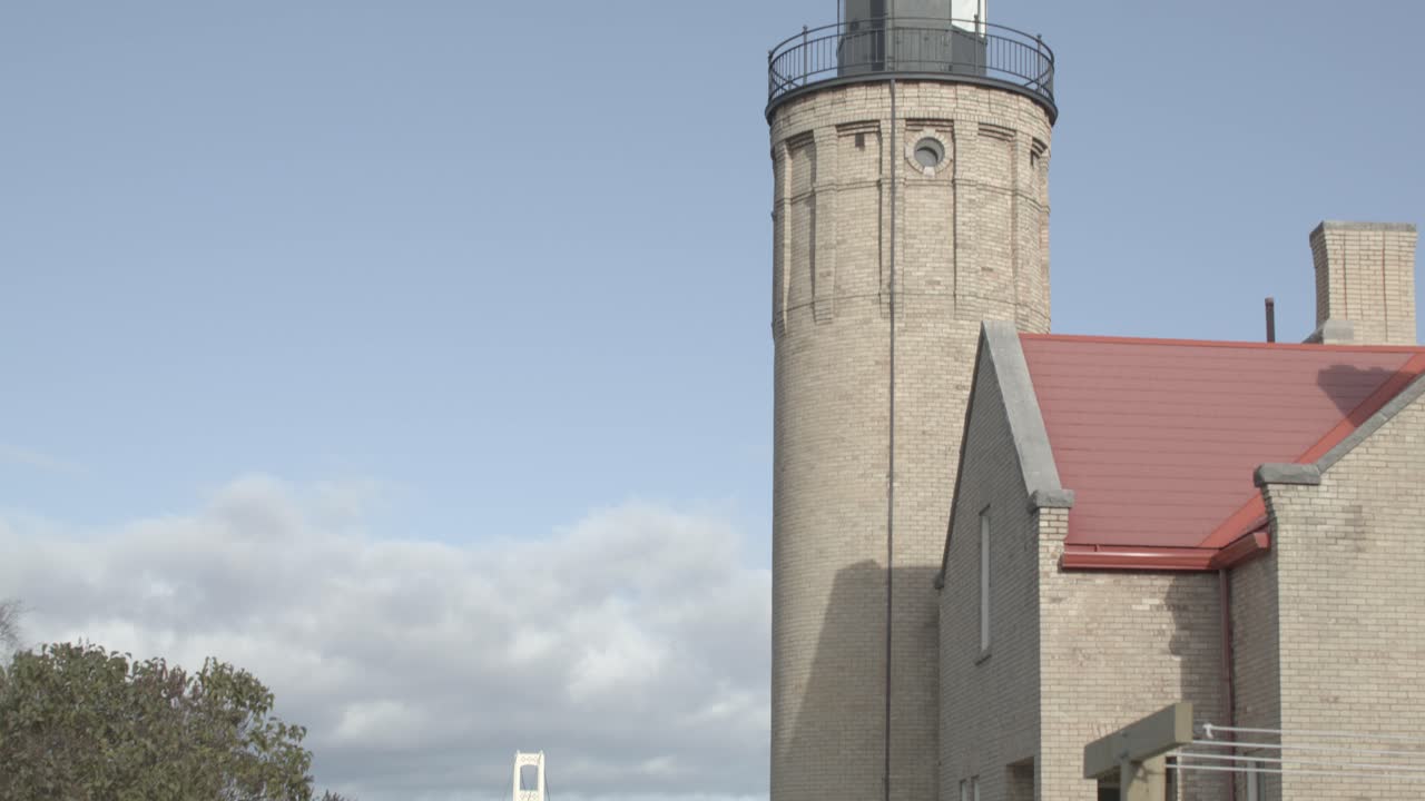 cerca de la parte superior del antiguo faro de mackinac point en la ciudad de mackinaw, michigan con inclinación hacia abajo a la valla de piquete blanca en primer plano y el puente de mackinac en el fondo con el dolly moviéndose de derecha a izquierda