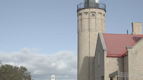 Close-up-of-top-of-Old-Mackinac-Point-lighthouse-in-Mackinaw-City,-Michigan-with-tilt-down-to-white-picket-fence-in-foreground-and-Mackinac-Bridge-in-background-with-dolly-moving-right-to-left