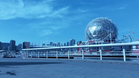 Loop-Lady-Trotar-Vista-Trasera-A-Lo-Largo-Del-Muelle-Frente-Al-Mar-De-Vancouver-Fondo-De-La-Aldea-Olímpica-Mundo-De-La-Ciencia-Horizonte-De-La-Ciudad-Moderna-En-Un-Día-Soleado-De-Adoquines-Con-Nubes-Claras-Ella-Es-Rubia-Vestida-De-Blanco-Gris