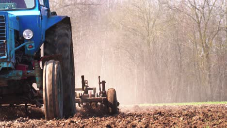 granjero conduce un viejo tractor soviético y cultiva un campo agrícola polvoriento