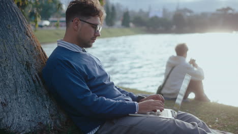 man sitting by tree outdoors using laptop