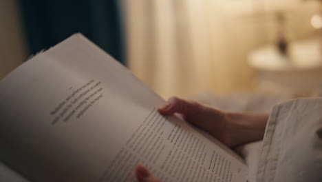 closeup hands turning page indoors. female student reading book at cozy home.