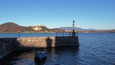 establishing static shot of fishing boat moored on lake maggiore in arona facing fortress of angera