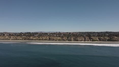 A-beautiful-aerial-drone-shot,-drone-flying-towards-the-coast-and-a-neighborhood-with-mountains-in-the-background,-Carlsbad-State-Beach---California