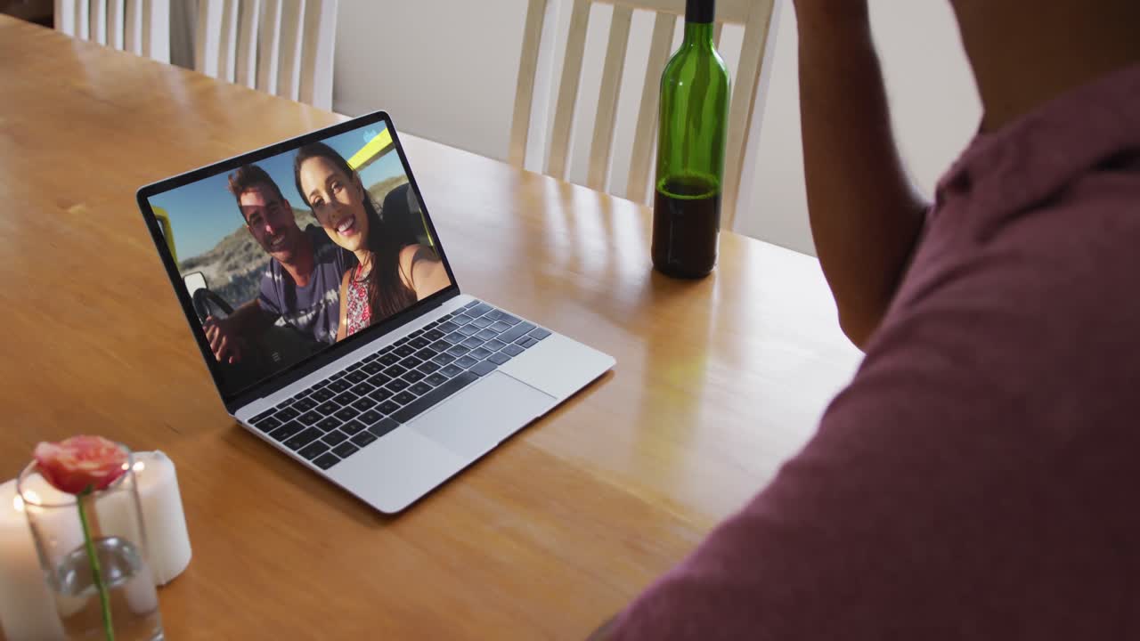 Mixed race man sitting at table using laptop making video call with friends