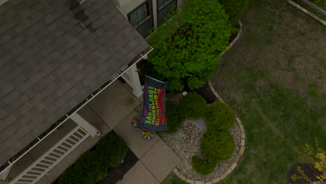 aerial over house with rainbow flag flying from front porch with a boom down towards the flag as it waves in the breeze in slow motion