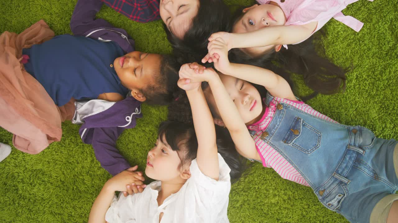 Multi ethnic Group of children lying in circle on green grass, Top view of kids paly together in living room at home.