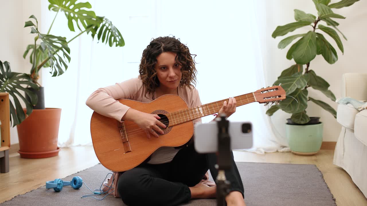 Woman musician playing acoustic guitar recording online lesson at home