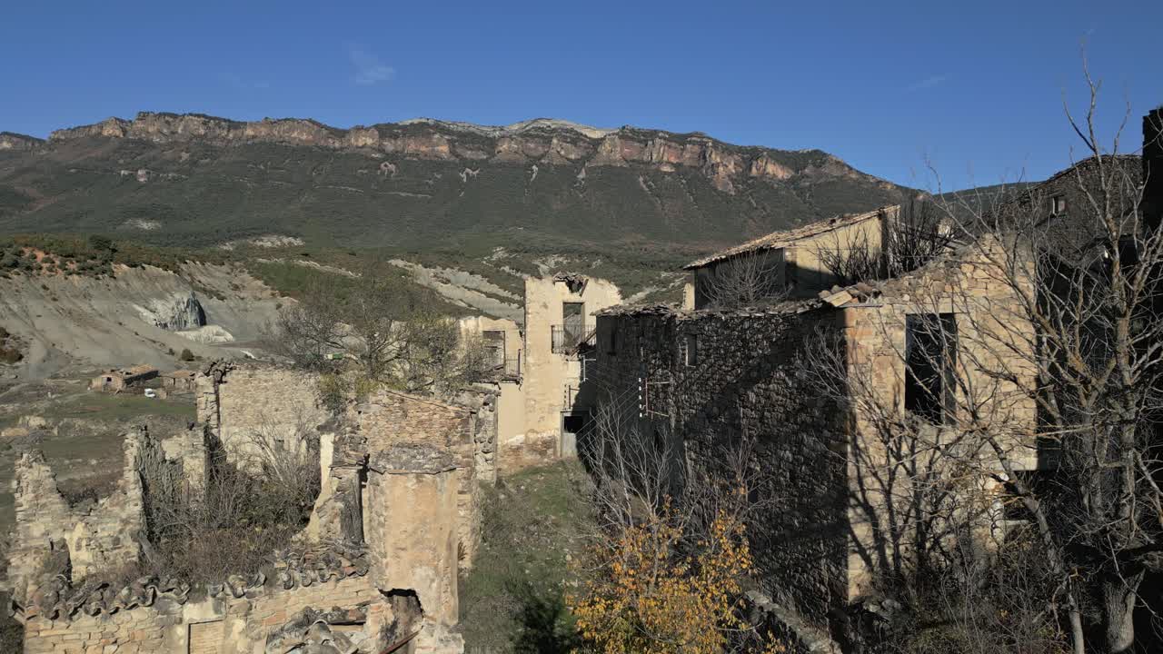 Vista panoramica della città fantasma abbandonata di Esco, un villaggio desolato con case in pietra in rovina, immerso nelle pittoresche montagne dell'Aragona, Spagna, contro un cielo azzurro limpido.