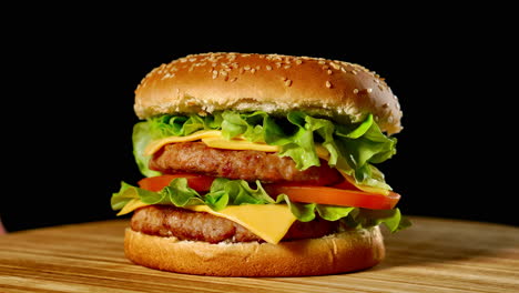 Fresh-appetizing-hamburger-rotating-on-black-background.-Seamless-loopable-shot,-4k.