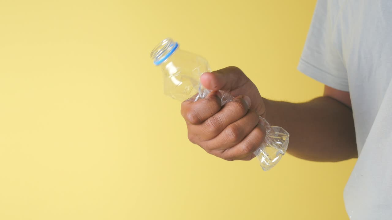 Hand crushing a plastic bottle against a yellow background