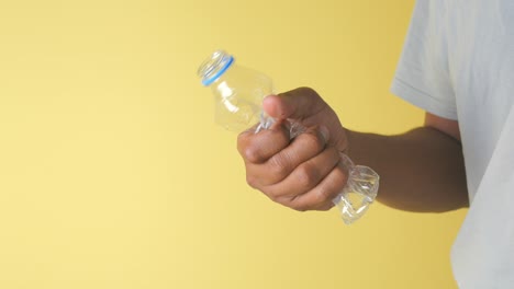 hand crushing a plastic bottle against a yellow background