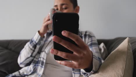 mujer usando un teléfono inteligente y tomando café en la sala de estar