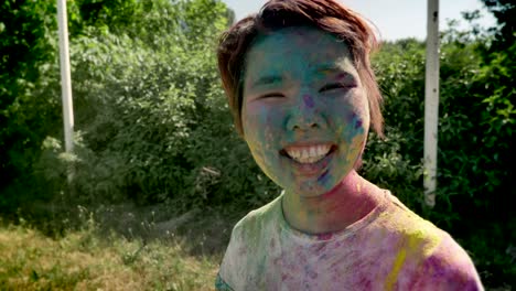 young cheerfyl asian girl in colors is thrown with colourful powder on holi festival in daytime in summer, color concept