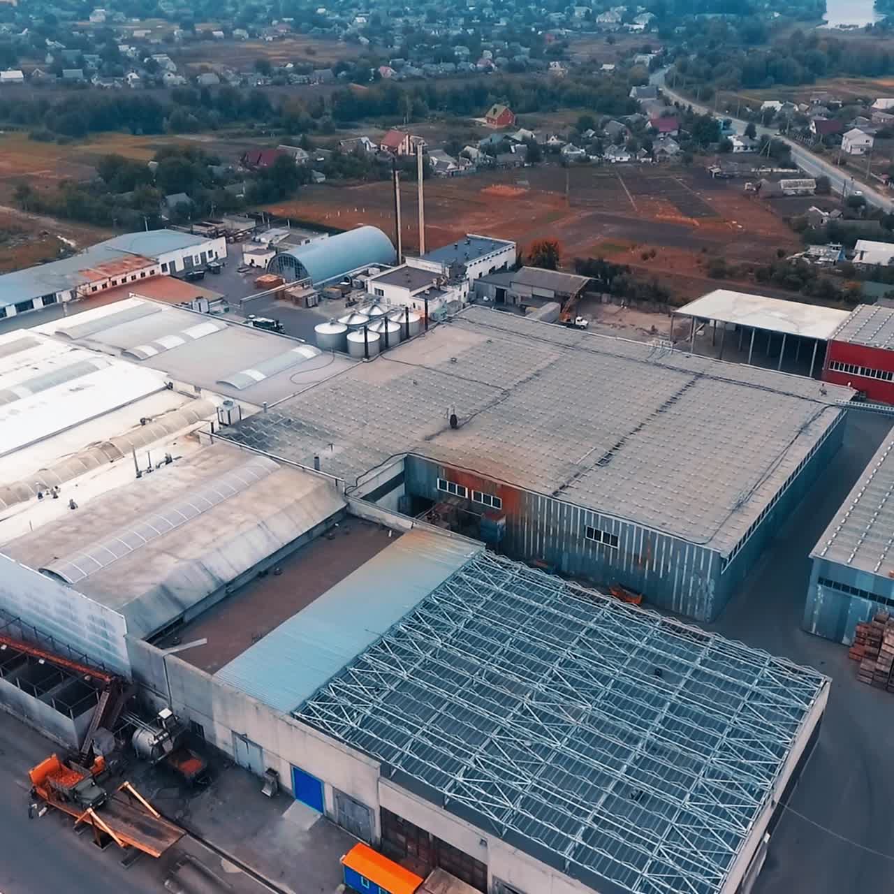 Large industrial zone with metal hangars and tanks. Huge country area with village houses and farmlands at backdrop