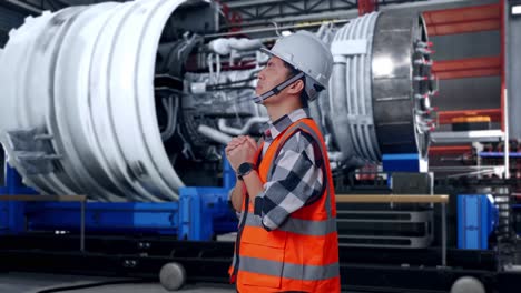 side view of asian male engineer with safety helmet pray for something while standing with airplane engine maintenance conducted, analytics checking the turbine