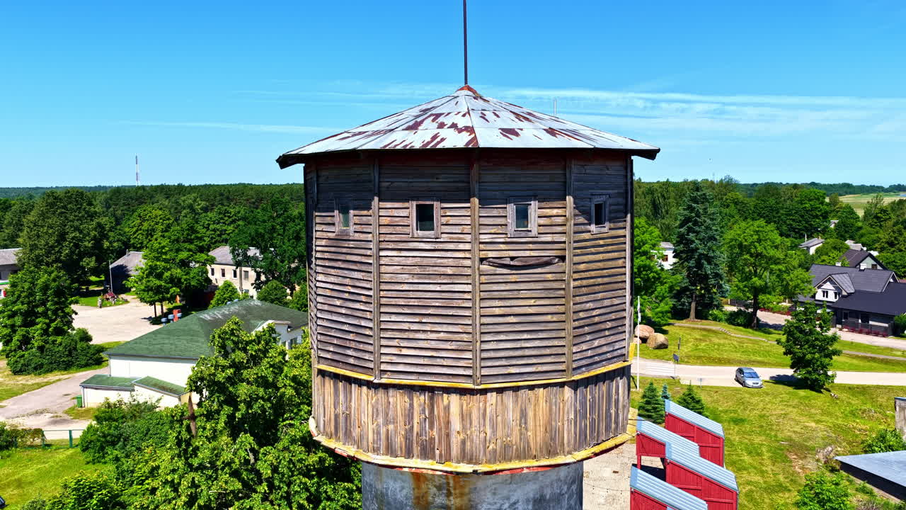 Aerial view of an old wooden water tower surrounded by greenery in Latvia, showcasing its weathered roof and unique architecture from above