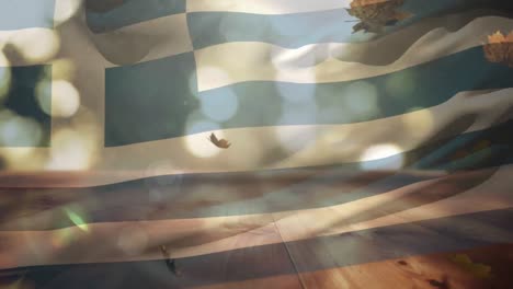 Composición-Digital-De-Grecia-Ondeando-La-Bandera-Sobre-Las-Hojas-De-Otoño-Cayendo-Sobre-La-Superficie-De-Madera