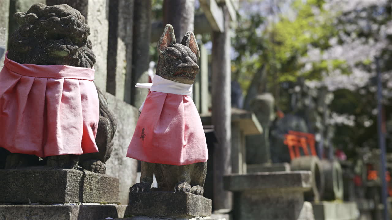 Stone fox statues adorned with red scarves at a beautiful shrine in Japan. This site showcases traditional architecture within a serene environment. Kyoto, Japan, Fushimi Inari