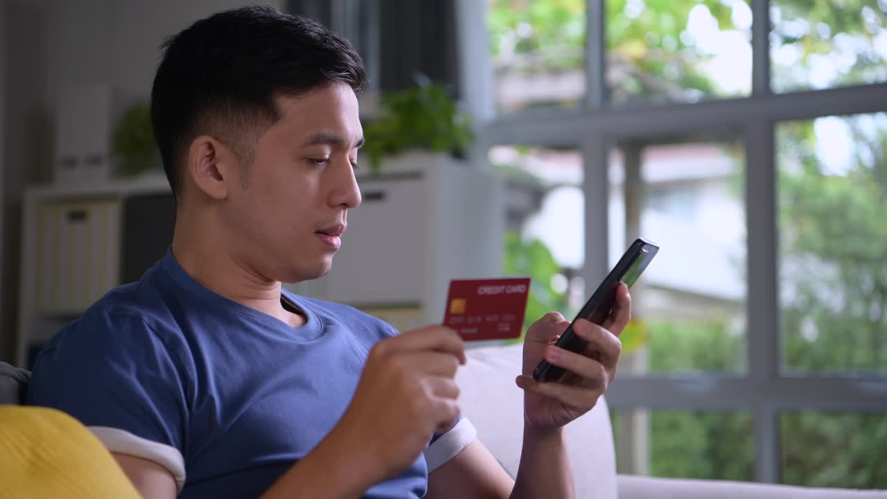 Pria Asia duduk nyaman di rumah menikmati dan menjelajahi belanja online serta pembayaran yang mudah dan nyaman menggunakan kartu kredit dengan aplikasi pembayaran online dan perbankan di ponsel pintar