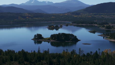 Early-fall-colors-Lake-Dillon-islands-Colorado-aerial-cinematic-drone-morning-view-Frisco-Breckenridge-Silverthorne-Ten-Mile-Range-calm-reflective-water-yellow-Aspen-trees-pan-up-reveal-movement