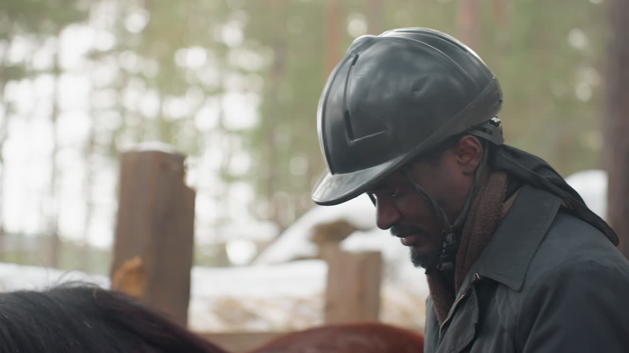cheerful rider wearing protective headgear interacts calmly with horse amidst winter landscape, content man with helmet shares relaxed moment with his horse in snowy paddock setting