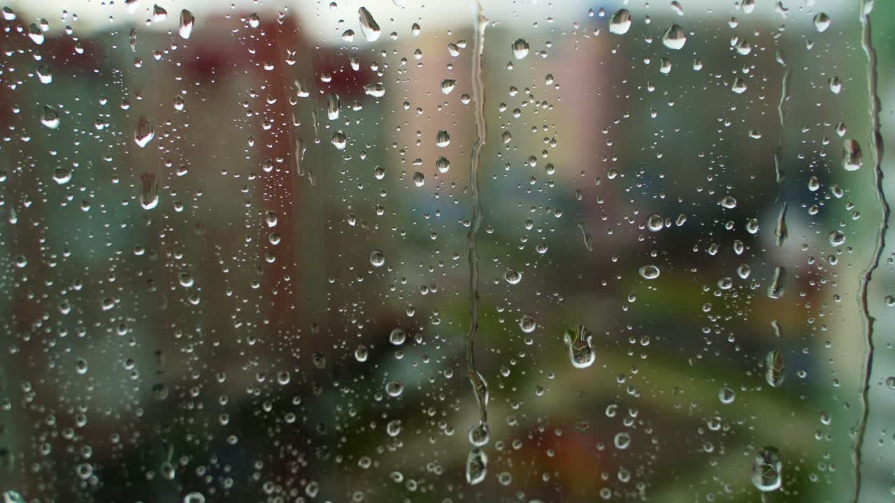 Droplets on glass during rain. Raindrops falling on the window on blur background outside. Wet weather. Close-up.