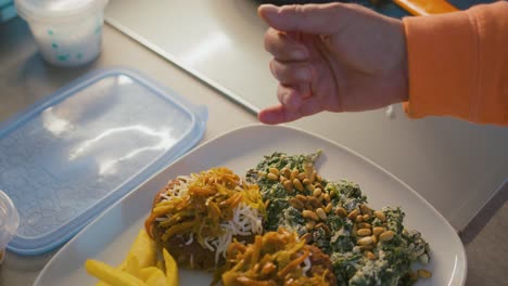 adding pine nuts to spinach with cheese, on a plate where there are also burgers with onion, peppers, and cheese, and french fries