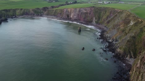 Aerial-moving-shot-of-a-bay-and-sea-stack-at-The-Copper-Coast-Waterford-Ireland-on-a-Winter-afternoon