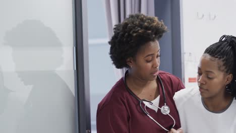 African-american-female-doctor-helping-female-patient-walking-in-hospital-corridor,-slow-motion