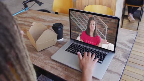 mujer tomando un bocadillo mientras hace una videollamada en una computadora portátil en una cafetería